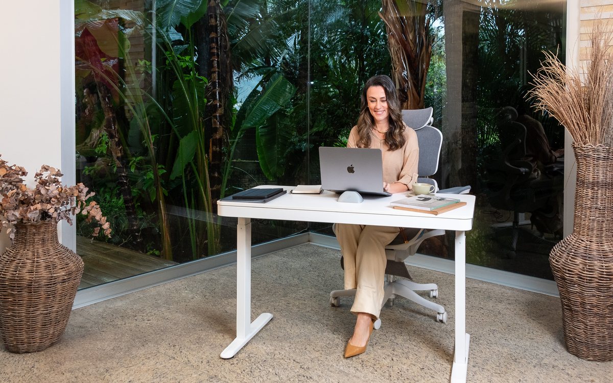 Mulher trabalhando no laptop numa mesa branca de frente para o jardim, na cadeira EOS