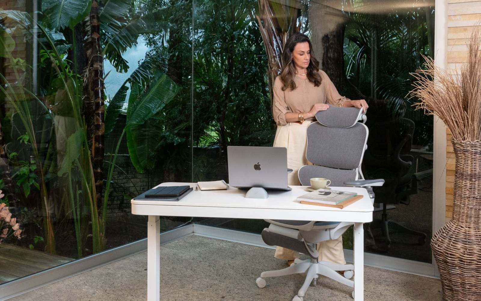 Mulher em pé ao lado da cadeira EOS, na mesa de trabalho montada, com a vegetação ao fundo.